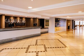 A hotel reception area with a reception desk, a wall-mounted TV, and a poster advertising amenities. -  Complexo Eco Cataratas Resort by SJ (Foz do Iguaçu)