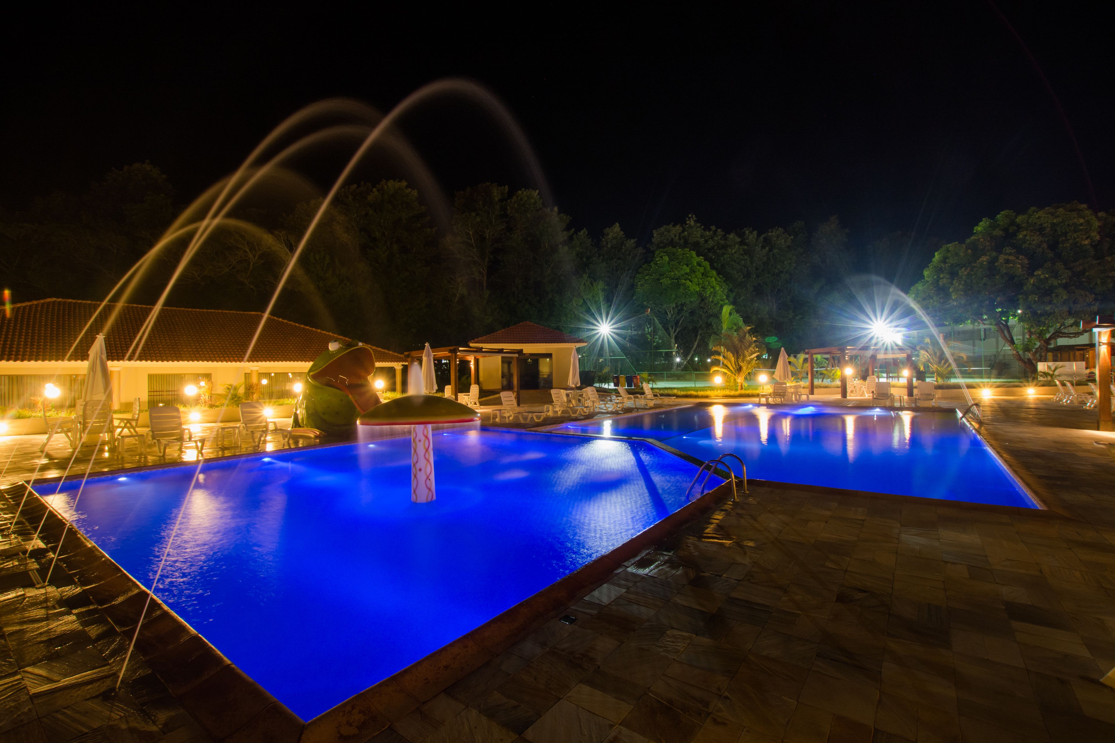 A nighttime swimming pool with water features and lounge chairs.