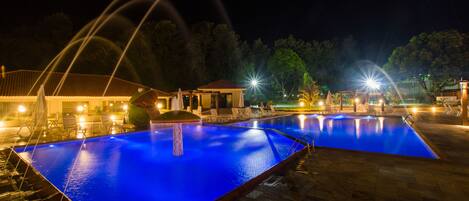A nighttime swimming pool with water features and lounge chairs.
