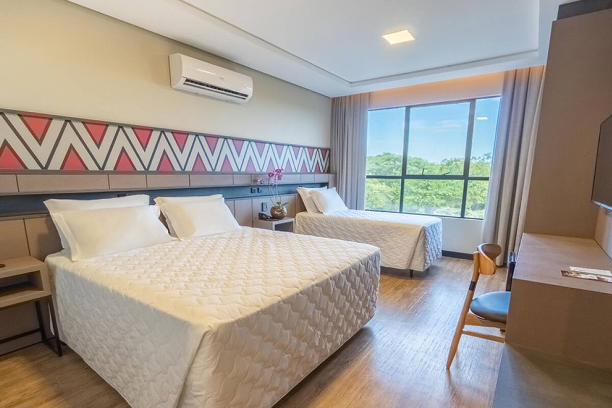 Une chambre d’hôtel avec deux lits, un bureau, une chaise, une télévision et une grande fenêtre donnant sur un beau paysage.
