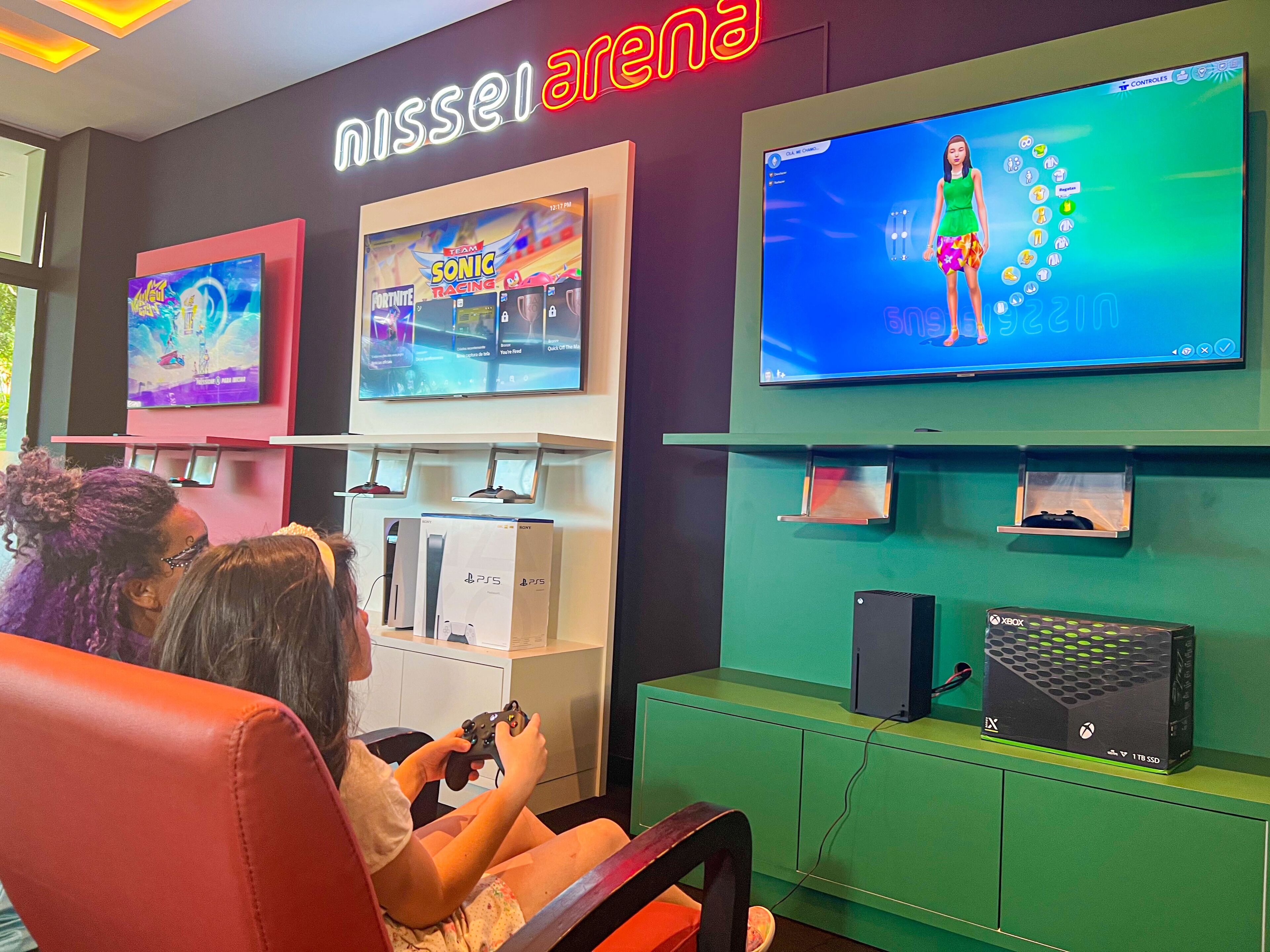 A gaming area with multiple screens displaying video games, a PlayStation 5 console, and an Xbox console.