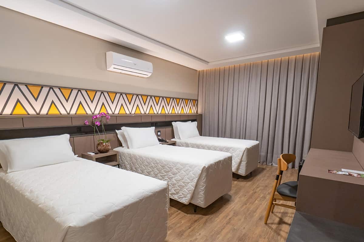 Une chambre d’hôtel avec deux lits, un bureau, une chaise, un appareil de climatisation et un téléviseur fixé au mur.