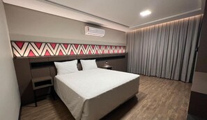 A modern hotel room with a large bed, a bedside table, a nightstand, a wall-mounted air conditioner, and a patterned headboard. -  Complexo Eco Cataratas Resort by SJ (Foz do Iguaçu)