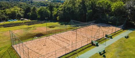 An outdoor tennis court surrounded by green grass and trees.