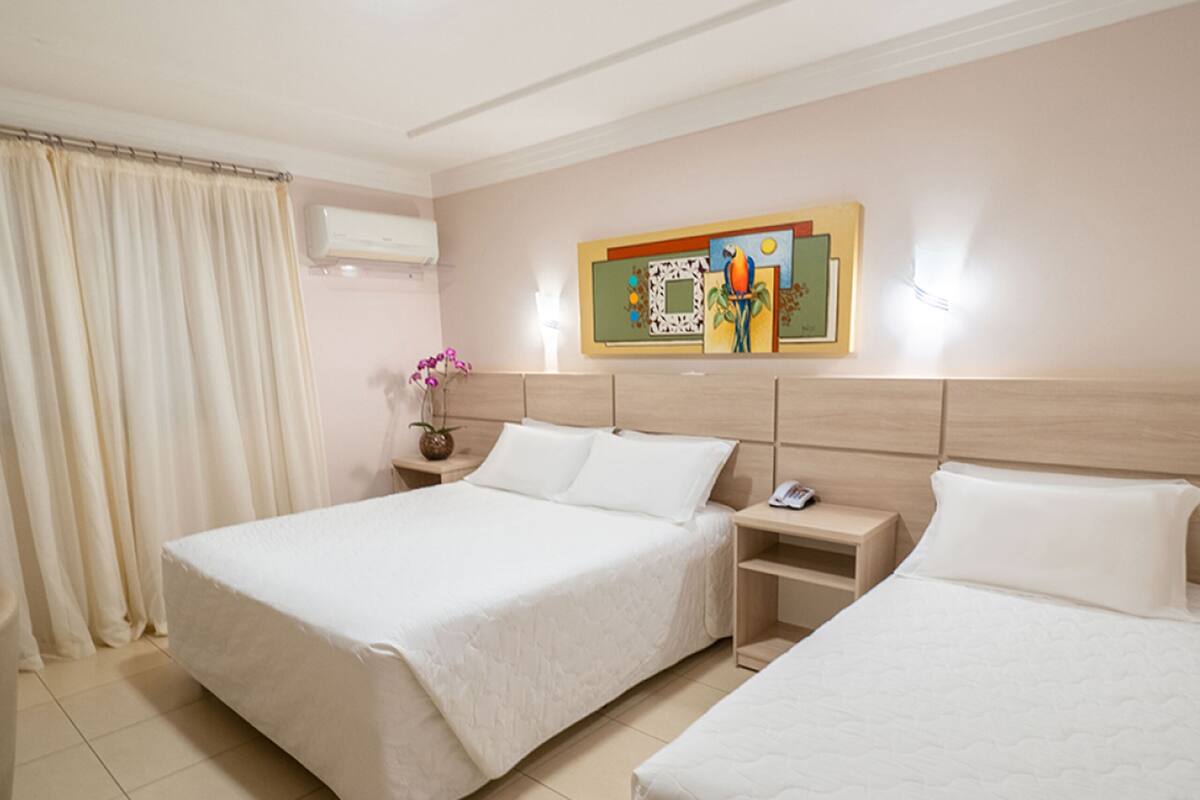 Une chambre d’hôtel avec deux lits, une table de chevet, un vase de fleurs et un tableau au mur.
