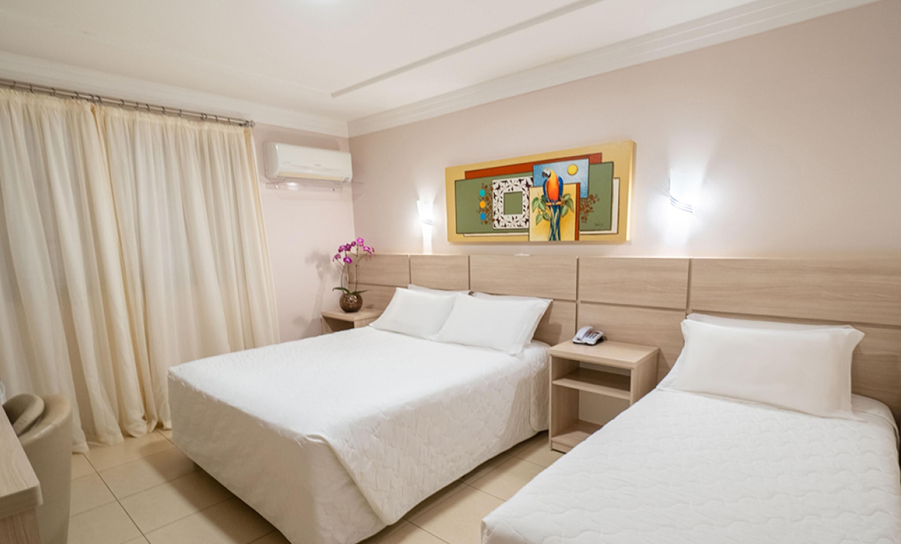 Ein Hotelzimmer mit zwei Betten, einem Nachttisch, einer Blumenvase und einem Bild an der Wand.