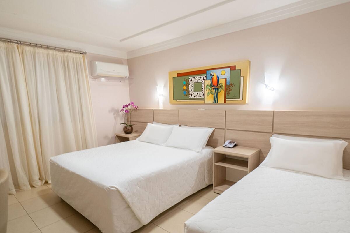 Une chambre d’hôtel avec deux lits, une table de chevet, un vase avec des fleurs et un tableau au mur.