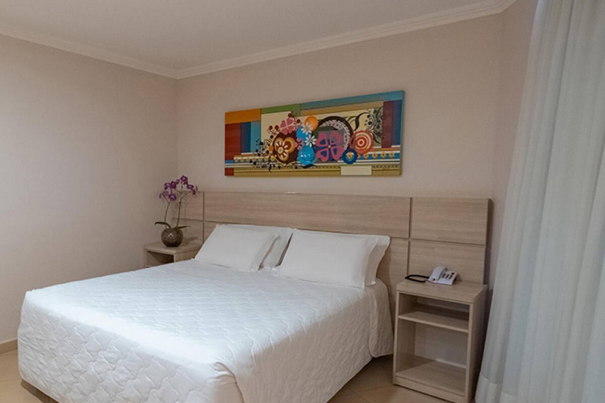 Une chambre à coucher avec un lit, une table de chevet, un vase de fleurs et un tableau coloré au mur.