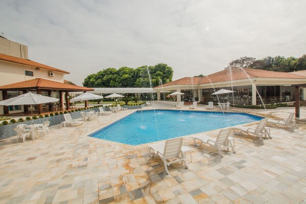 A swimming pool with lounge chairs and umbrellas, surrounded by a tiled patio area. -  Complexo Eco Cataratas Resort by SJ (Foz do Iguaçu)