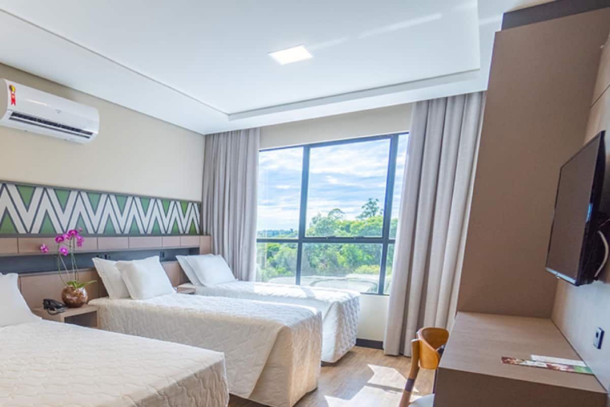 Une chambre d’hôtel avec deux lits, une télévision et une grande fenêtre donnant sur un paysage verdoyant.