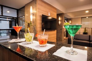 A bar area with three cocktails on the counter, a television mounted on the wall, and a modern interior design. - SJ Business - San Juan São Paulo (São Paulo)