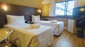 Habitación de hotel con dos camas, televisión, refrigerador pequeño y ventana con cortinas.