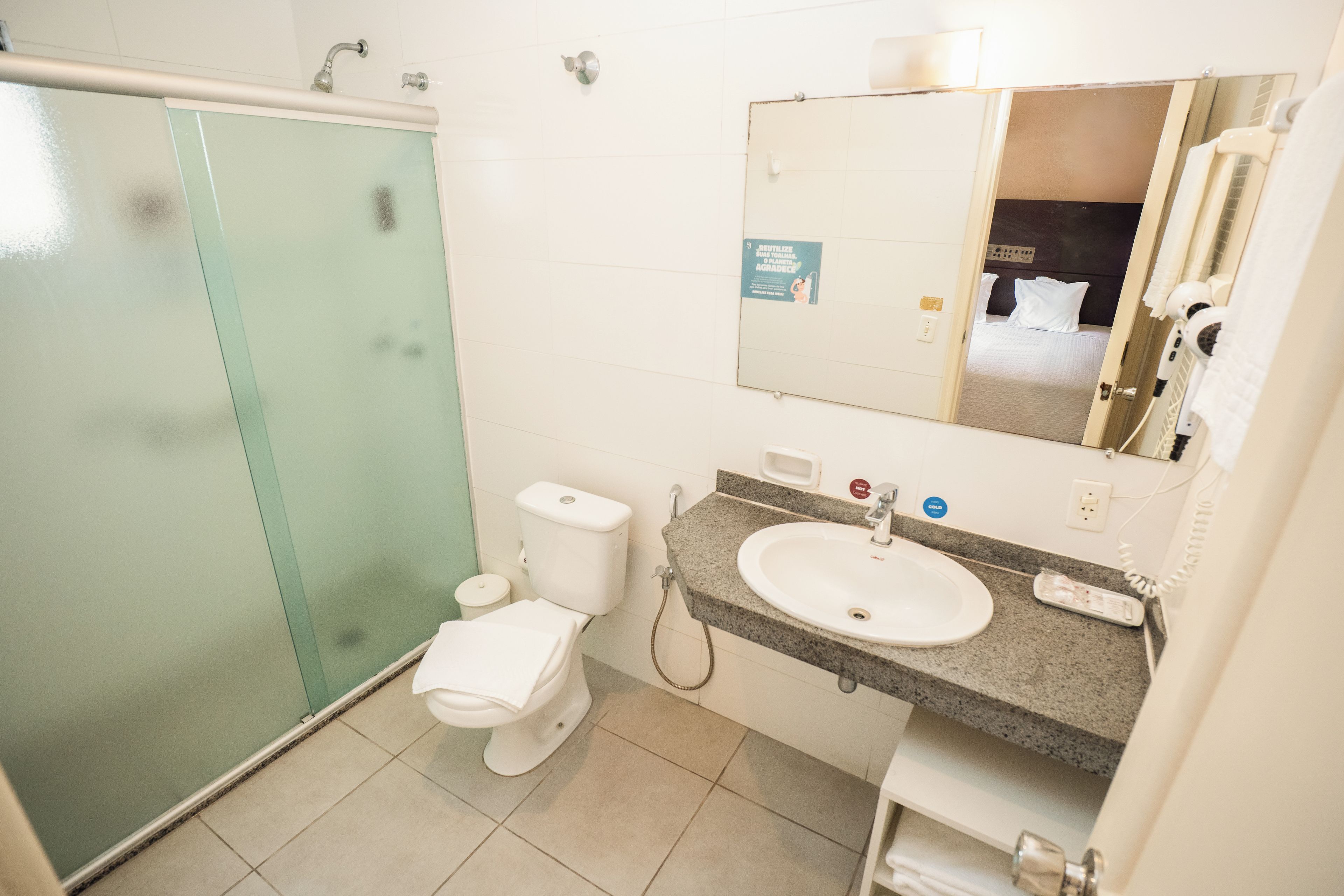 A bathroom with a glass shower enclosure, a toilet, a sink with a mirror, and a towel rack.