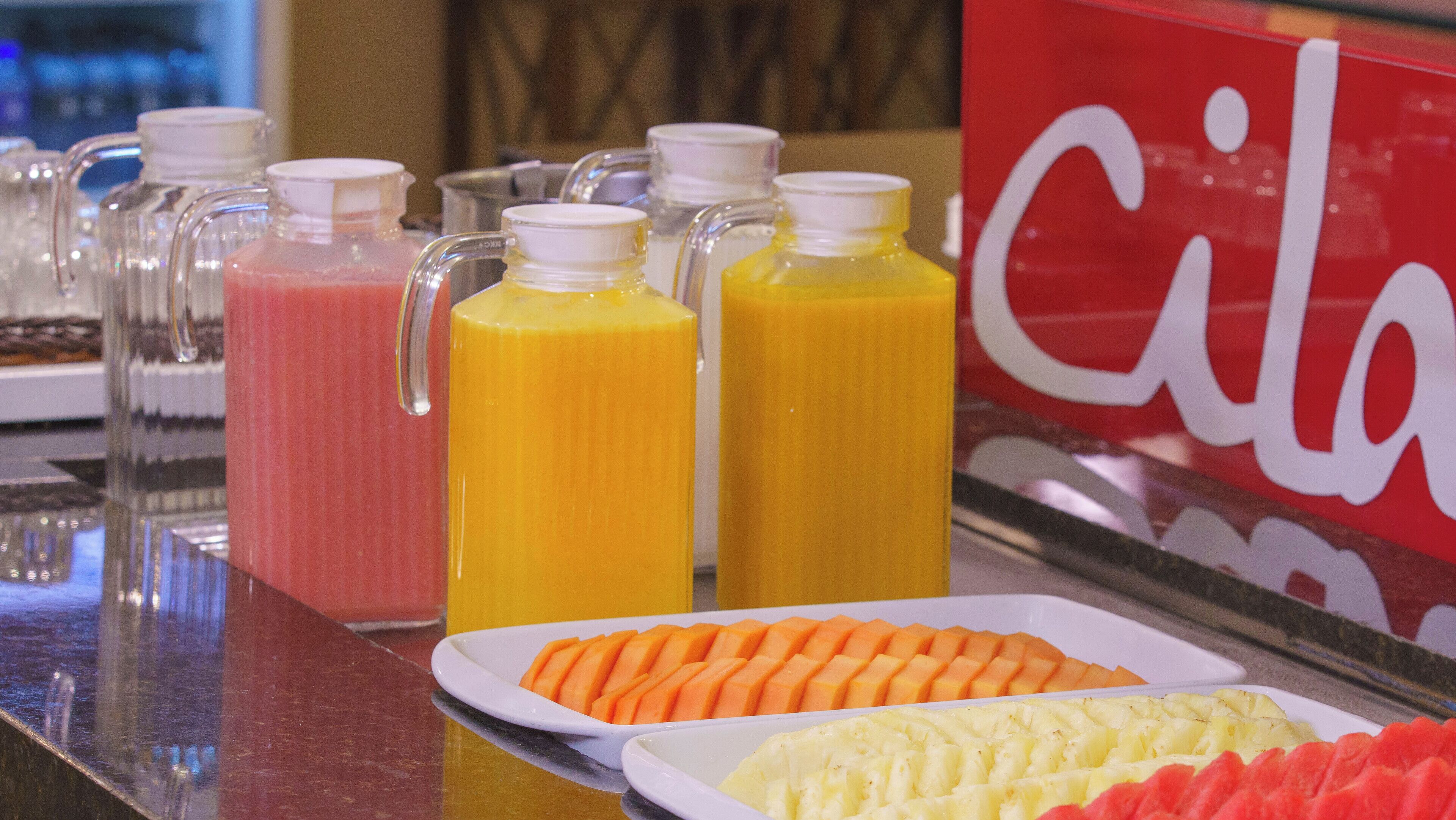 A buffet with various fruit juices and sliced fruits.
