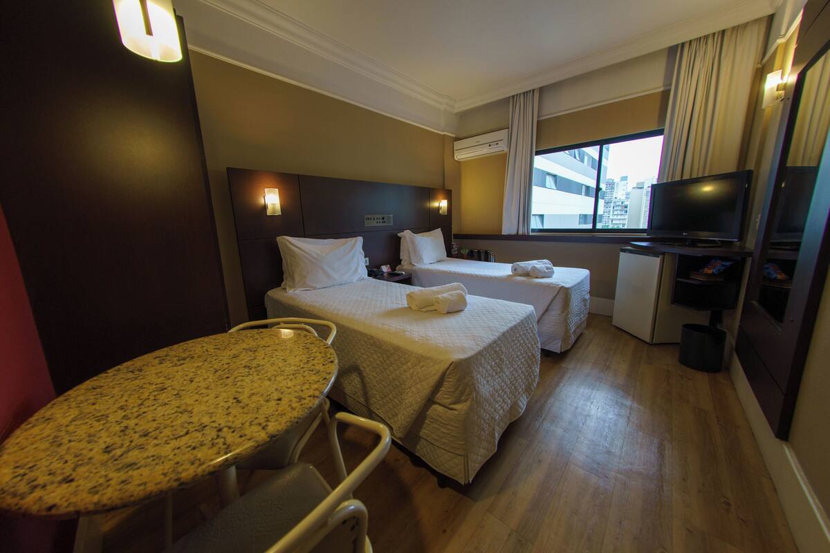 Een hotelkamer met twee bedden, een klein bureau, een televisie en een zithoek.