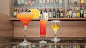 Tres cócteles sobre una barra con una estantería de botellas de licor al fondo.