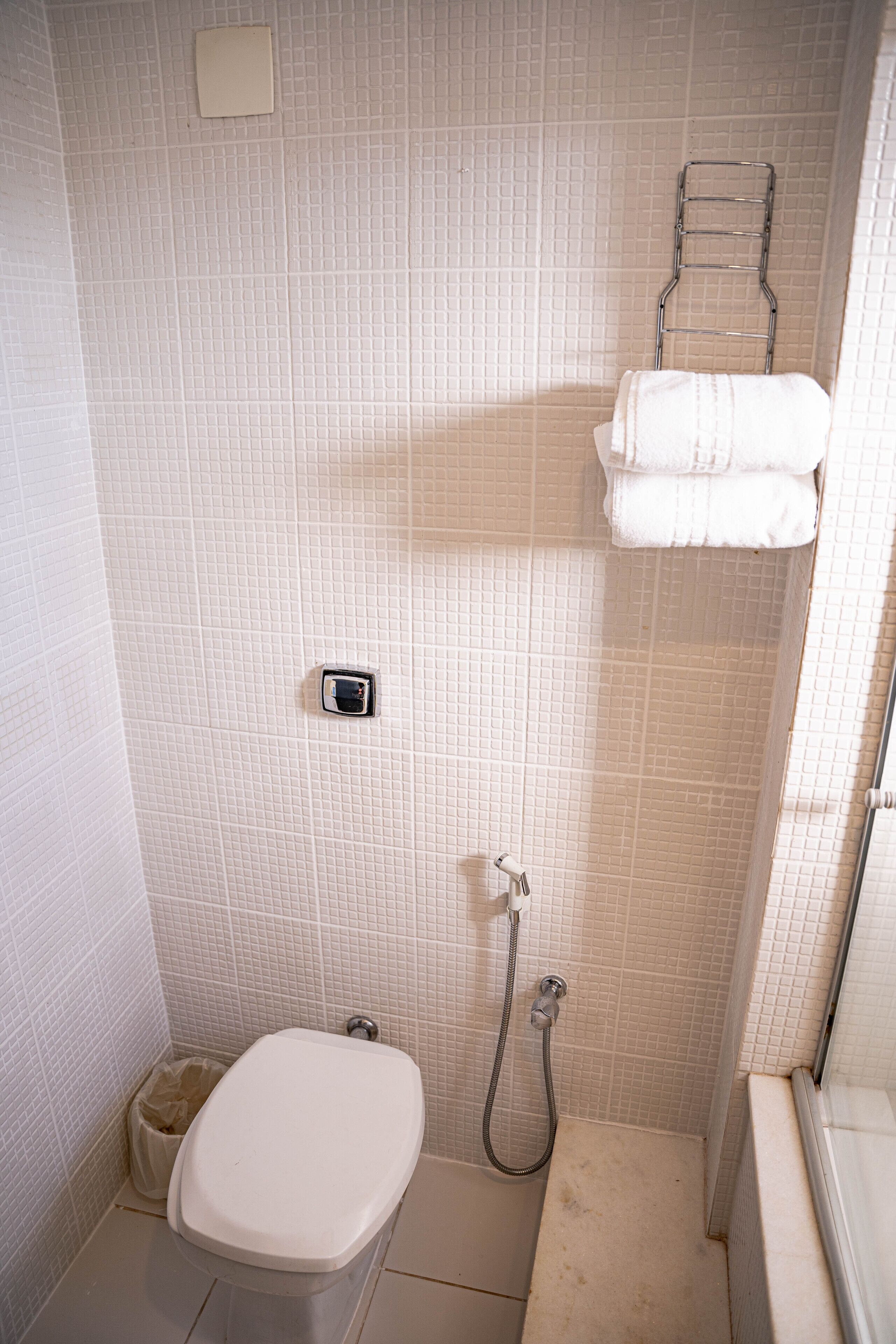A small, tiled bathroom with a toilet, a shower, and a towel rack.