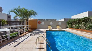 Una piscina con escalera metálica, sillas de descanso y una palmera.