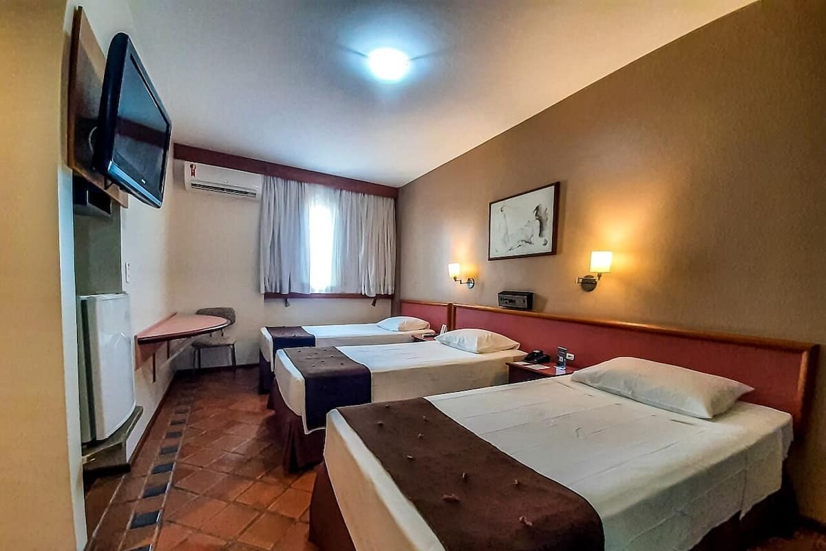 Ett hotellrum med tre enkelsängar, ett litet bord, en tv och en luftkonditioneringsanläggning.