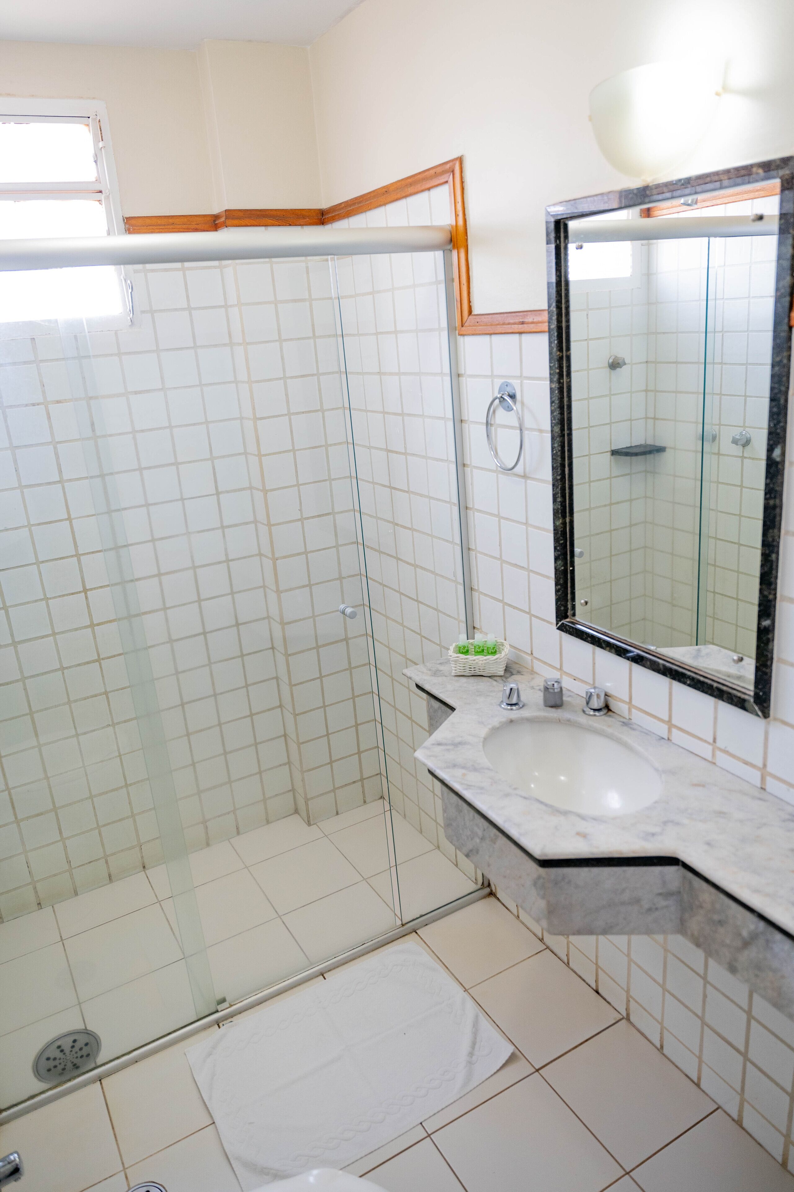 Uma casa de banho com cabine de chuveiro em vidro, lavatório com bancada de mármore e espelho com moldura preta.