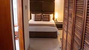 Una habitación de hotel con una cama grande, una mesita de noche con lámpara y un armario de madera.