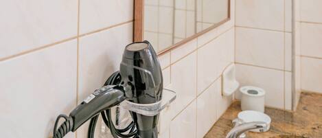A bathroom with a large mirror, a hairdryer, a sink, and a toilet paper holder.