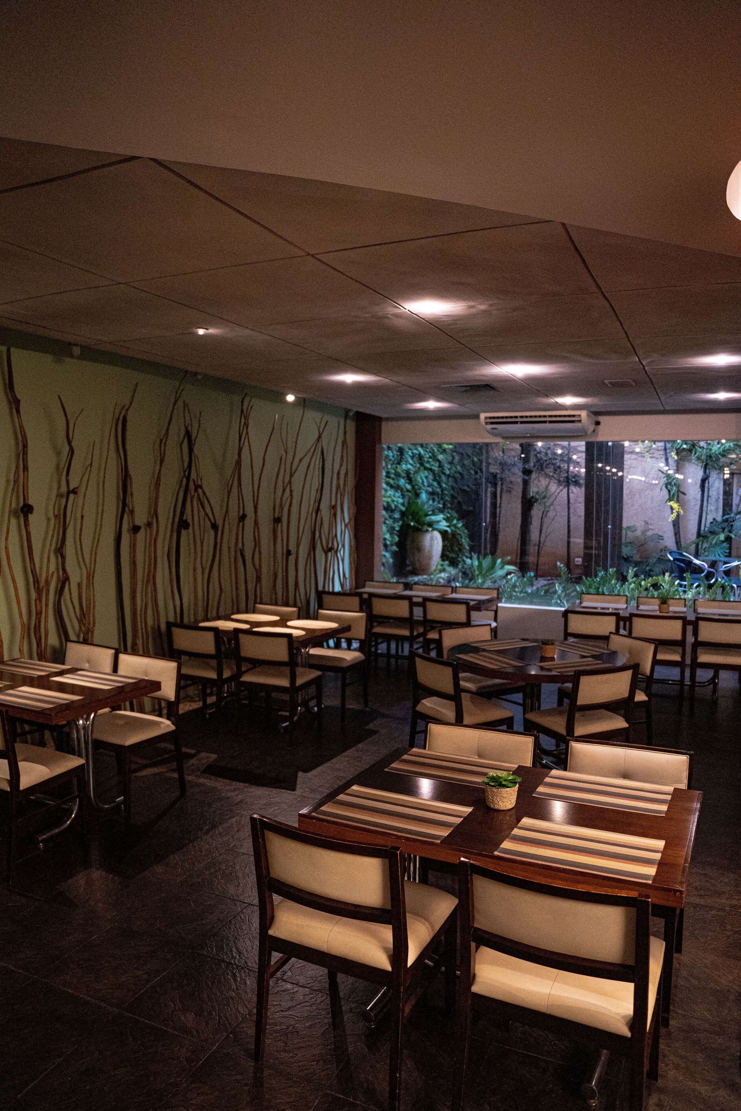 Un restaurante con varias mesas y sillas, un ventanal con vistas a zonas verdes e iluminación empotrada en el techo.