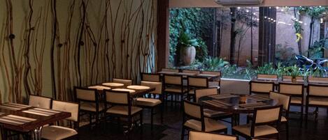 Un restaurante con varias mesas y sillas, un ventanal con vistas a zonas verdes e iluminación empotrada en el techo.