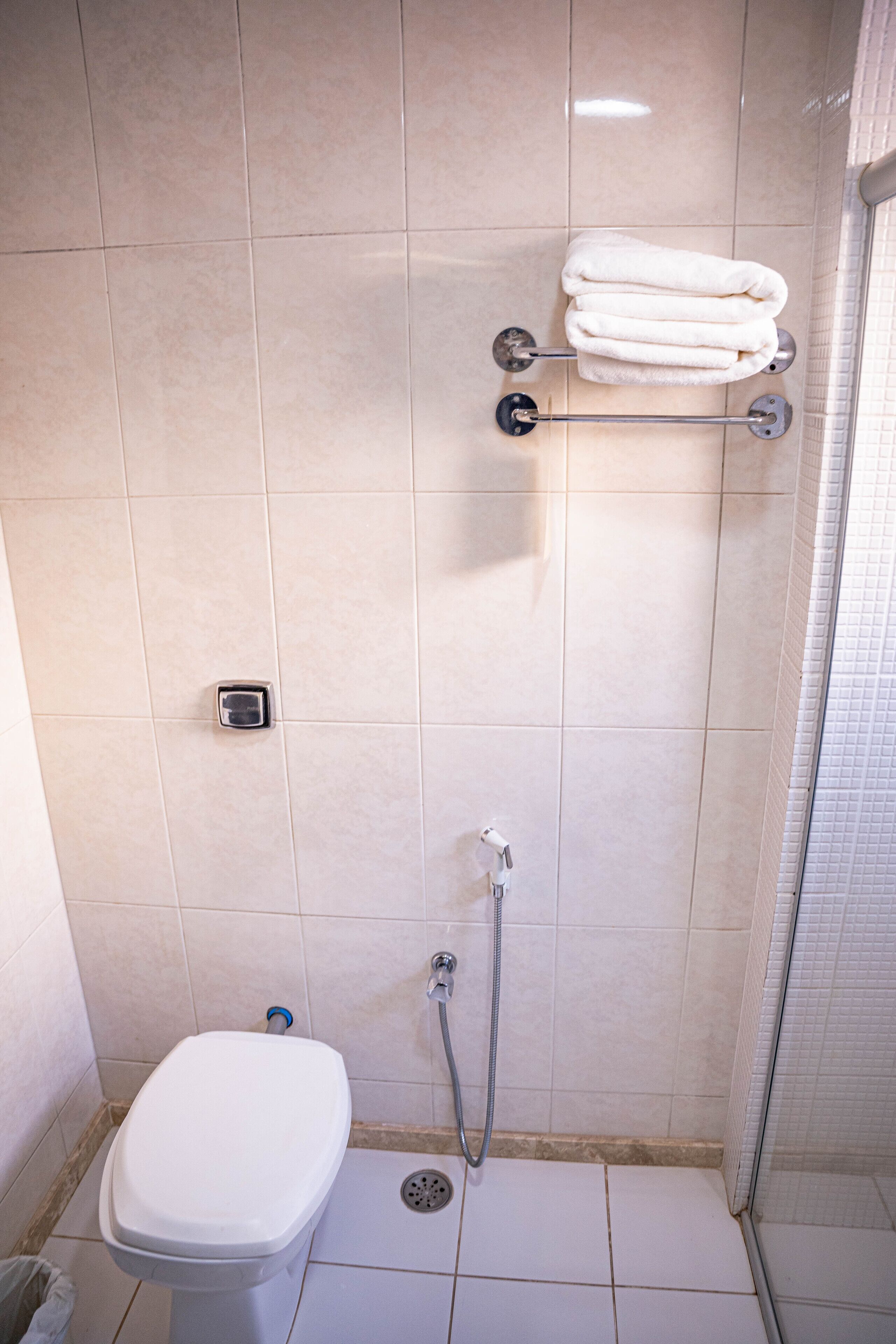 Et lille badeværelse med fliser, toilet, brusebad og et håndklædestativ.