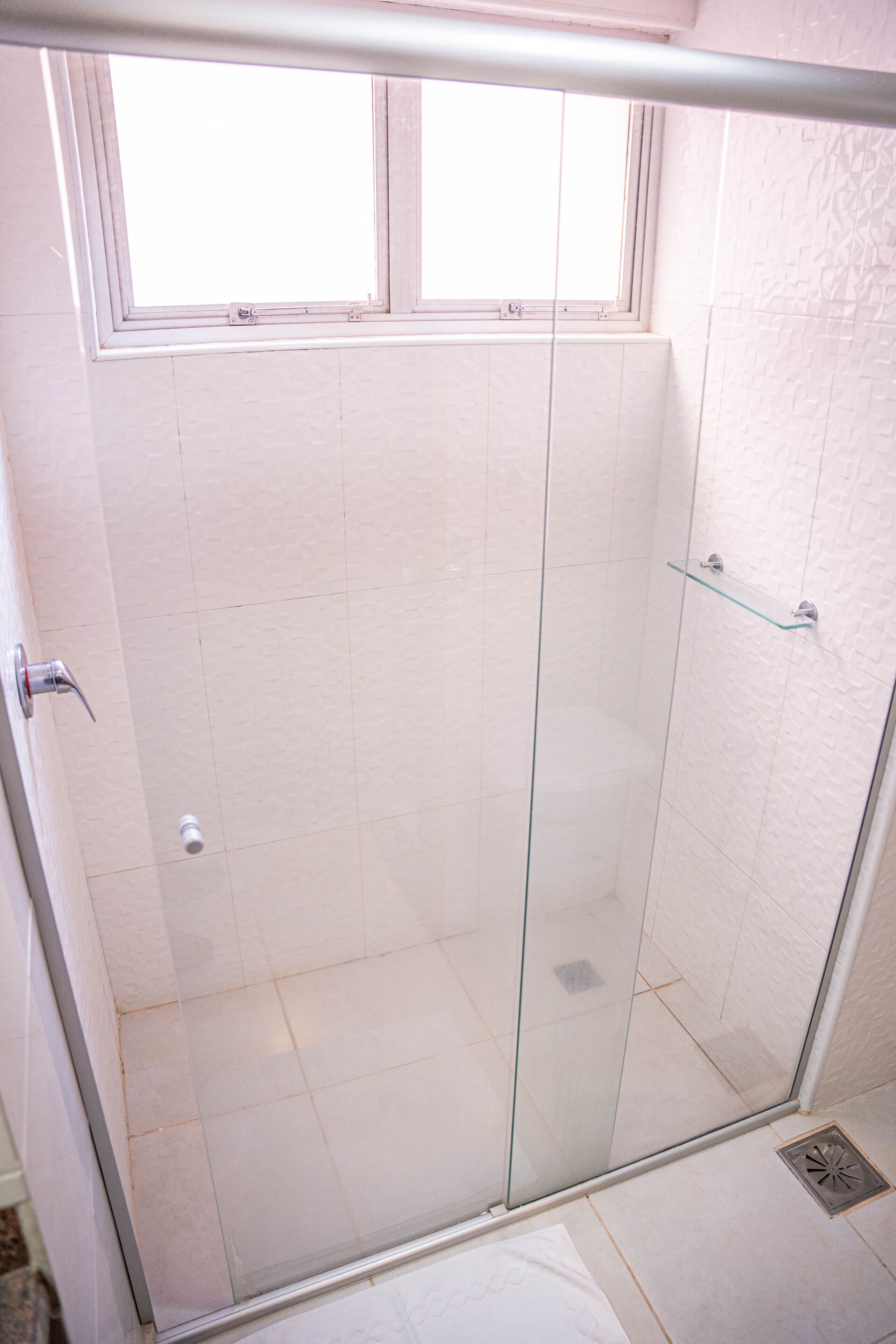 A glass-enclosed shower with a window above, tiled walls, and a metal handle on the door.