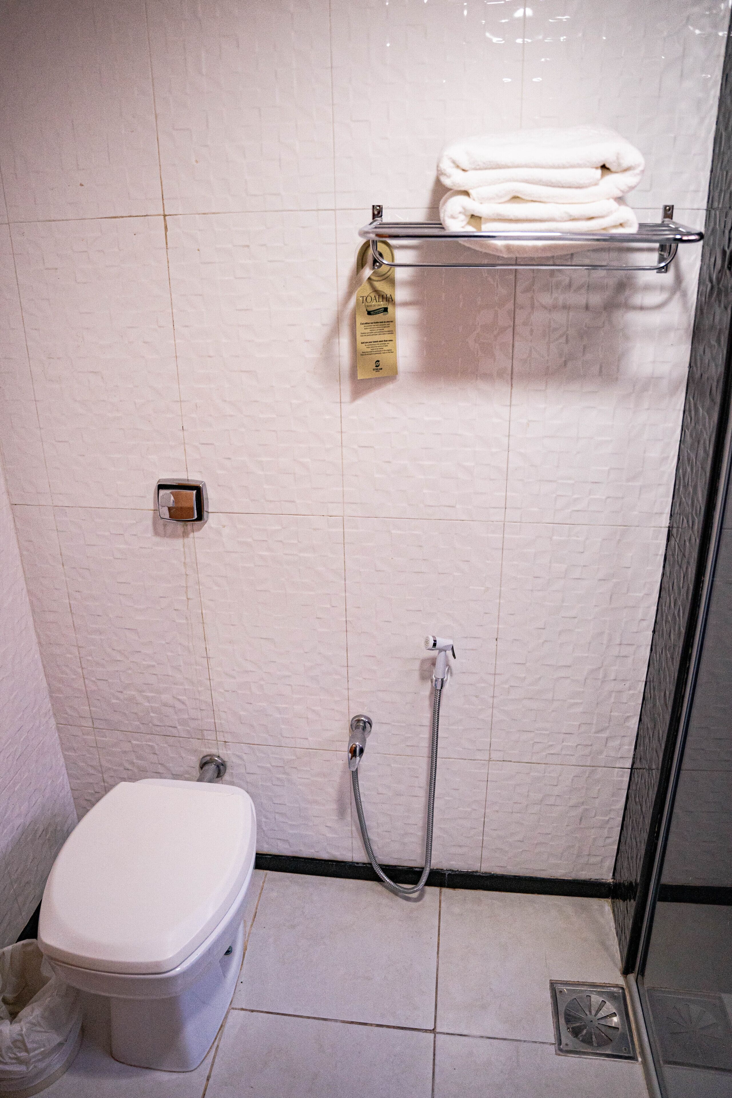 A small bathroom with a toilet, a shower, and a towel rack with folded towels.