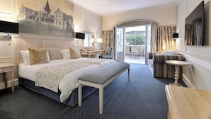 A hotel room with a large bed, a bench, a desk, a chair, a TV, and a view of the outside. - Swakopmund Hotel (Swakopmund)
