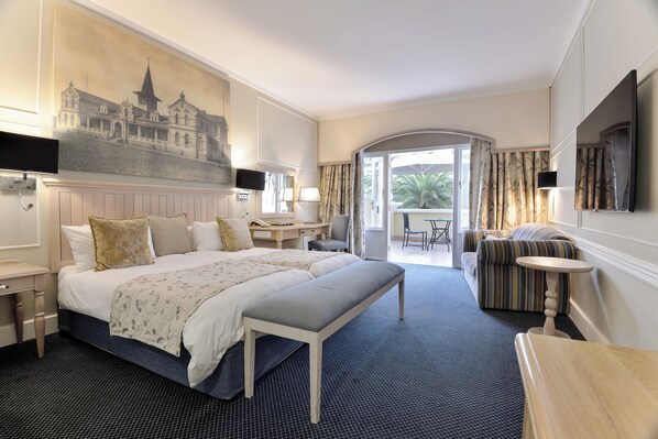 Une chambre d’hôtel avec un grand lit, une banquette, un bureau, une chaise, une télévision et une vue sur l’extérieur.