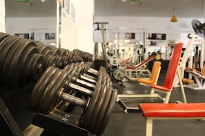 Une salle de sport avec plusieurs rangées de haltères, des appareils de musculation et un banc rouge.