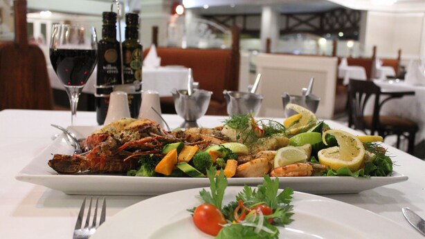 A dining table with a seafood dish, a glass of red wine, and a bottle of olive oil. - Swakopmund Hotel (Swakopmund)