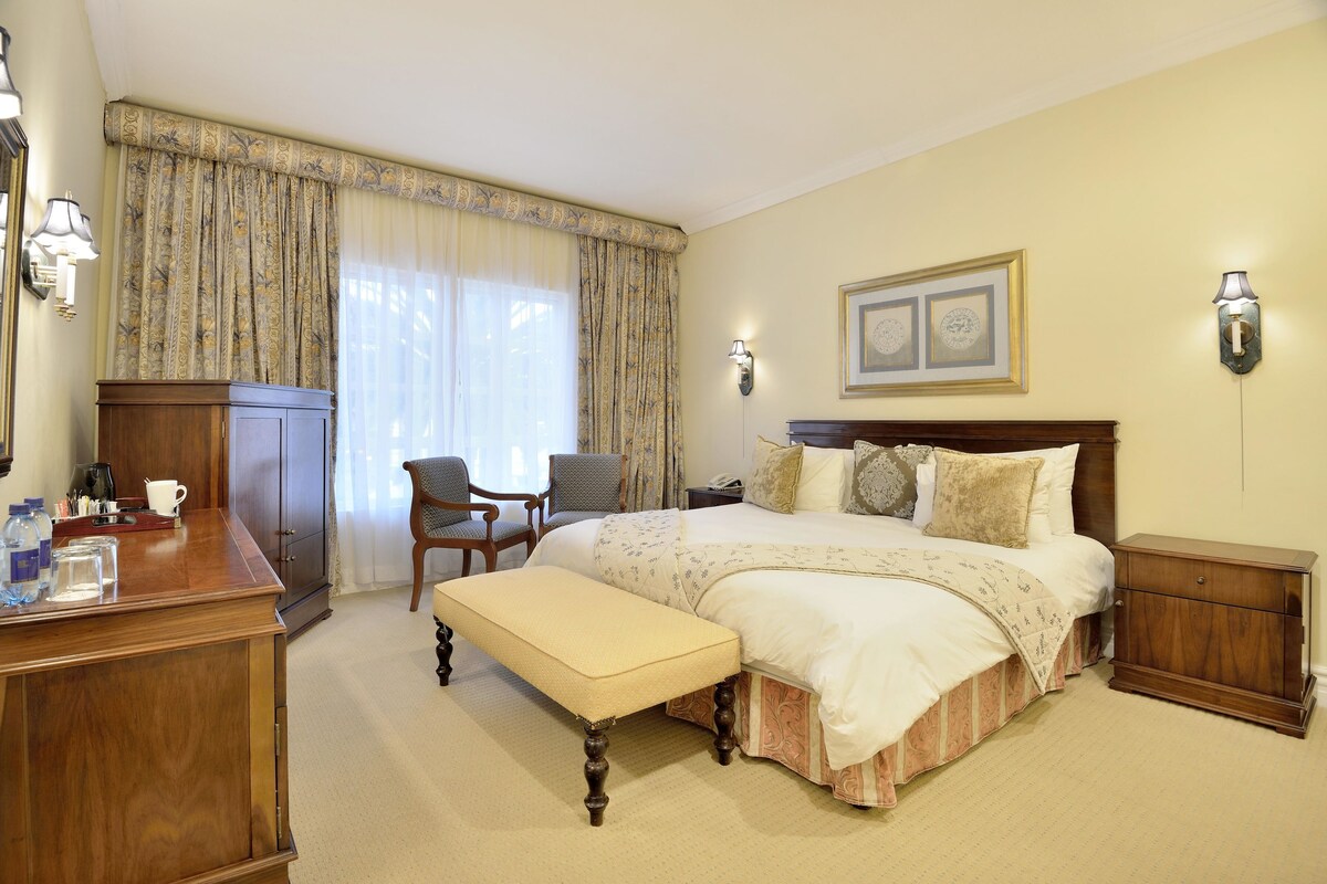 Een hotelkamer met een groot bed, een houten bureau, een stoel, een bankje en een nachtkastje.