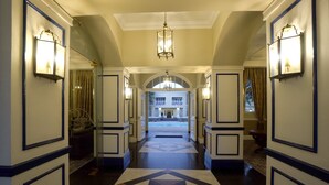 A hotel hallway with a geometric patterned floor, wall-mounted sconces, and a chandelier. - Swakopmund Hotel (Swakopmund)