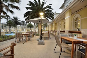 Un patio al aire libre con mesas y sillas, palmeras y un edificio con ventanas arqueadas.