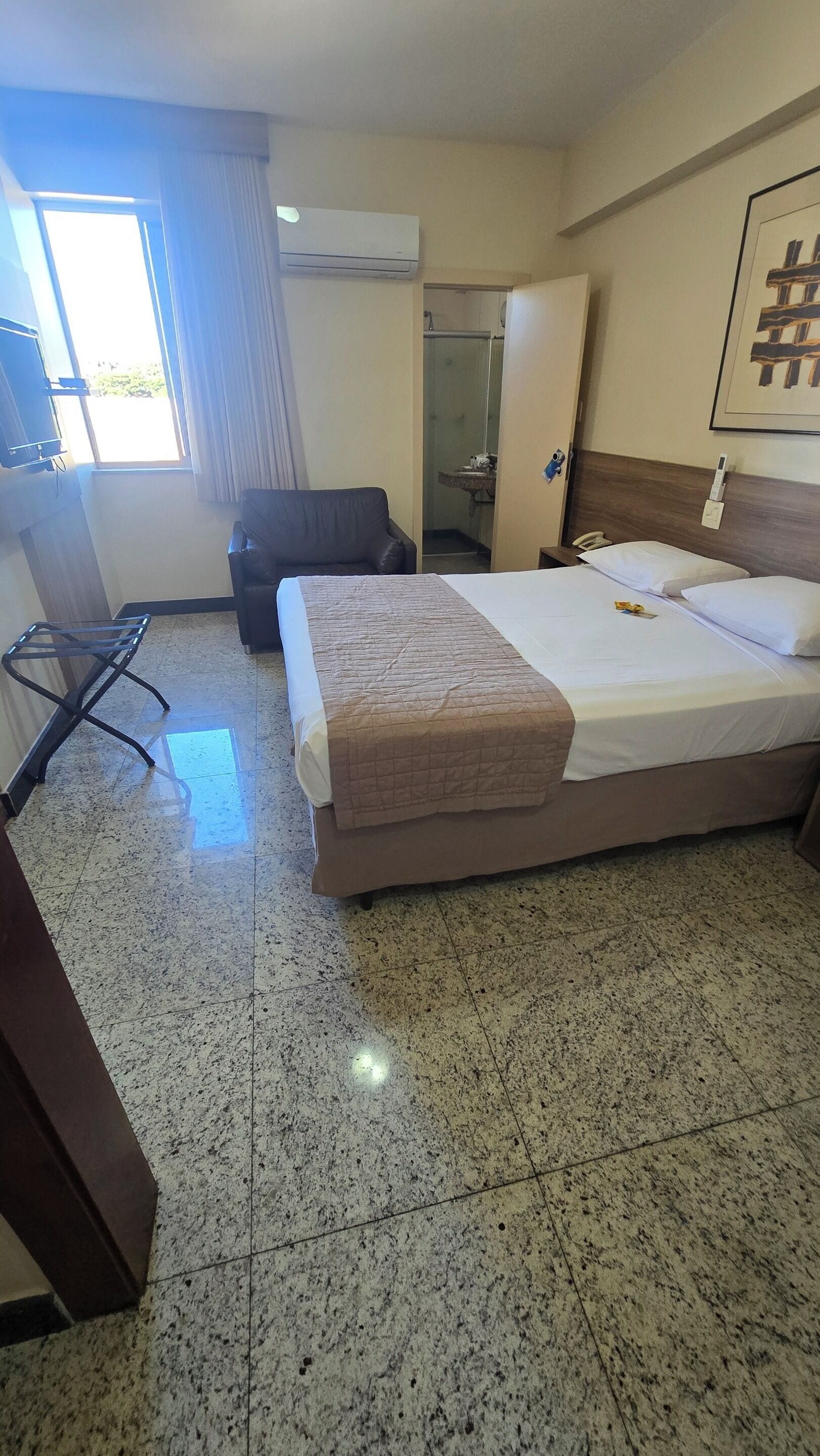 Une chambre d’hôtel avec un lit, une chaise, un bureau et une salle de bain visible à travers une porte ouverte.