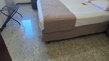 Hotellihuone, jossa on sänky, tuoli, työpöytä ja kylpyhuone, jotka näkyvät avoimesta ovesta.
