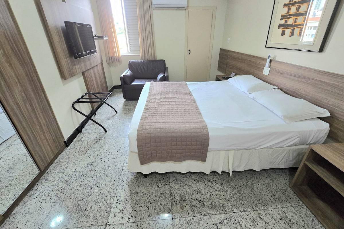 Een hotelkamer met een bed, een stoel, een televisie en een airconditioning.