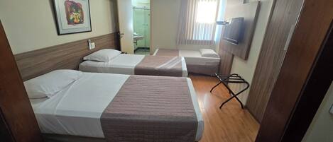 A hotel room with two beds, a small table, a TV, and a bathroom visible through an open door.