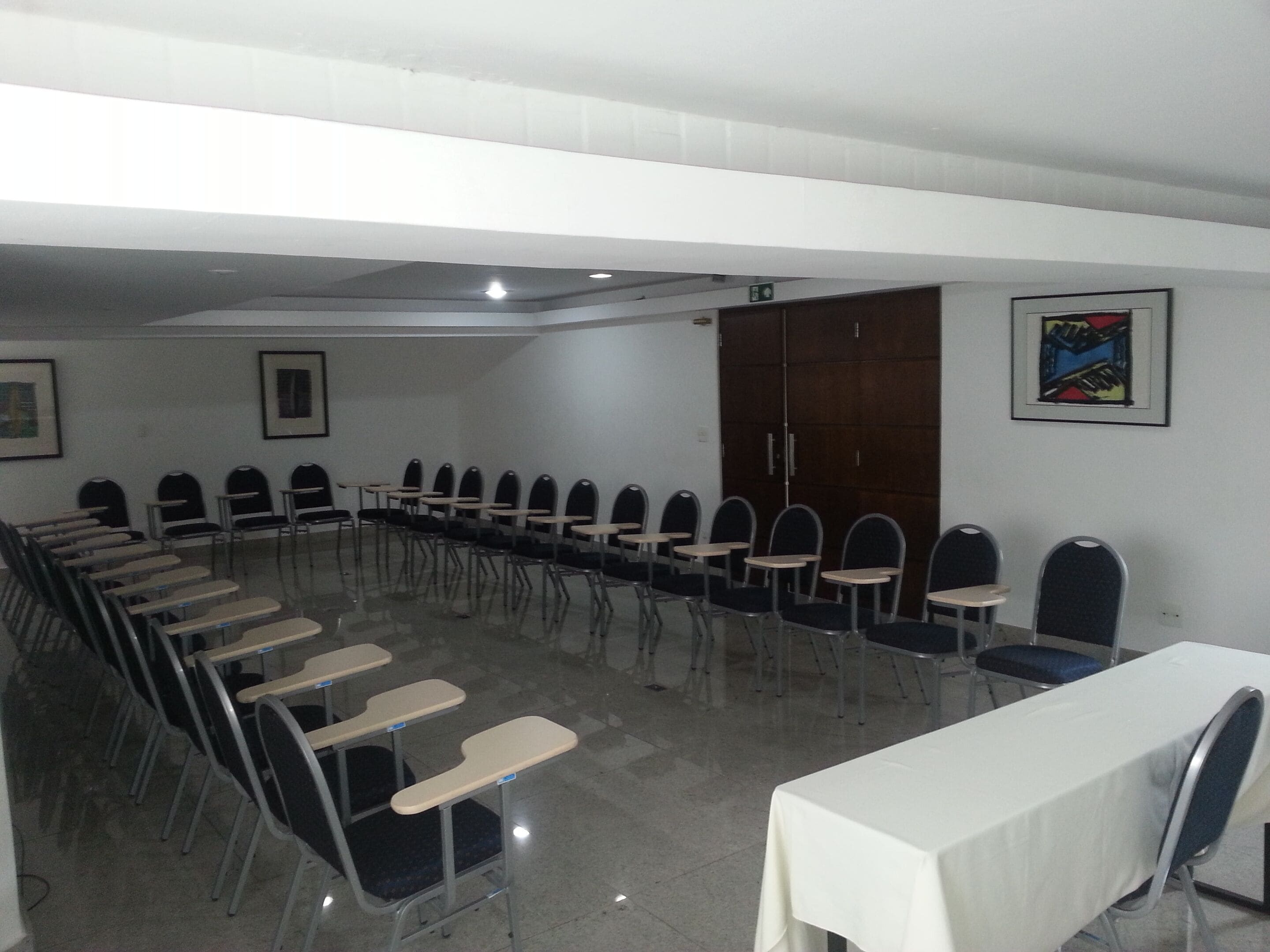 A conference room with rows of chairs and tables, a wooden door, and a framed picture on the wall.