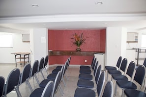 Un salón de conferencias con filas de sillas, una mesa de recepción y una planta decorativa.
