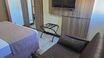Habitación de hotel con cama, sofá, televisión montada en una pared de madera y una mesita.