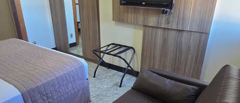 A hotel room with a bed, a sofa, a television mounted on a wooden wall, and a small table.