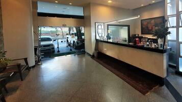 Uma área de recepção de hotel, com balcão, uma janela grande e entrada para estacionamento.