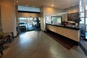 Zona de recepción de un hotel, con mostrador, un ventanal grande y acceso a estacionamiento.
