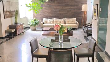 A modern living room with a glass dining table, leather sofas, and a large potted plant.