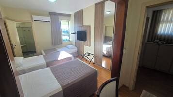 Quarto de hotel com duas camas, televisão, janela com cortinas e vista para a cidade.